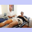 THW-Mannschaftsarzt Dr. Frank Pries erklrt Viktor Szilagyi, der auf einer Behandlungsliege liegt, anhand eines Modells die Verletzung im Knie.